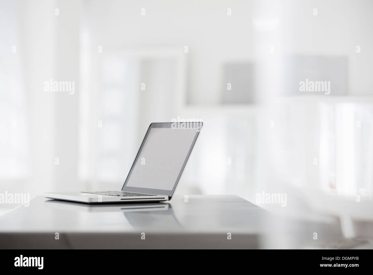 Office interior. A smooth shiny grey tabletop, and an open laptop computer. Stock Photo