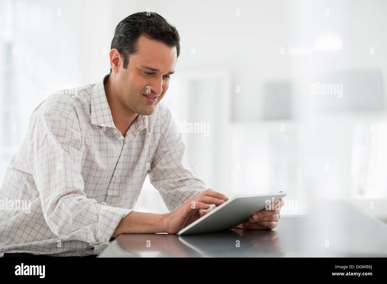 Office interior. A man seated at a table, using a digital tablet. Stock Photo