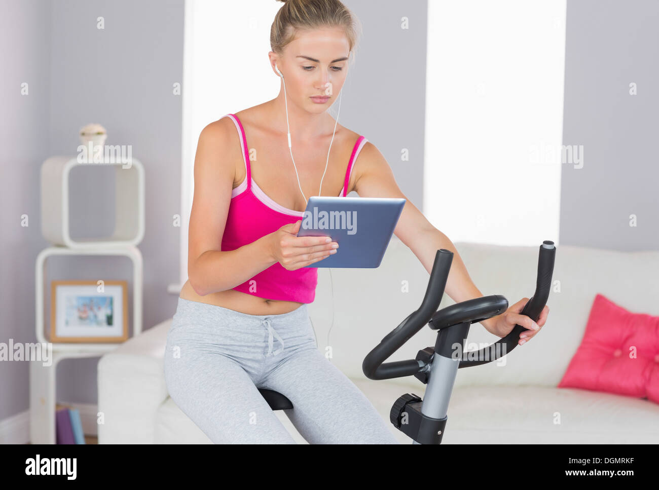 Sporty focused blonde training on exercise bike using tablet Stock Photo