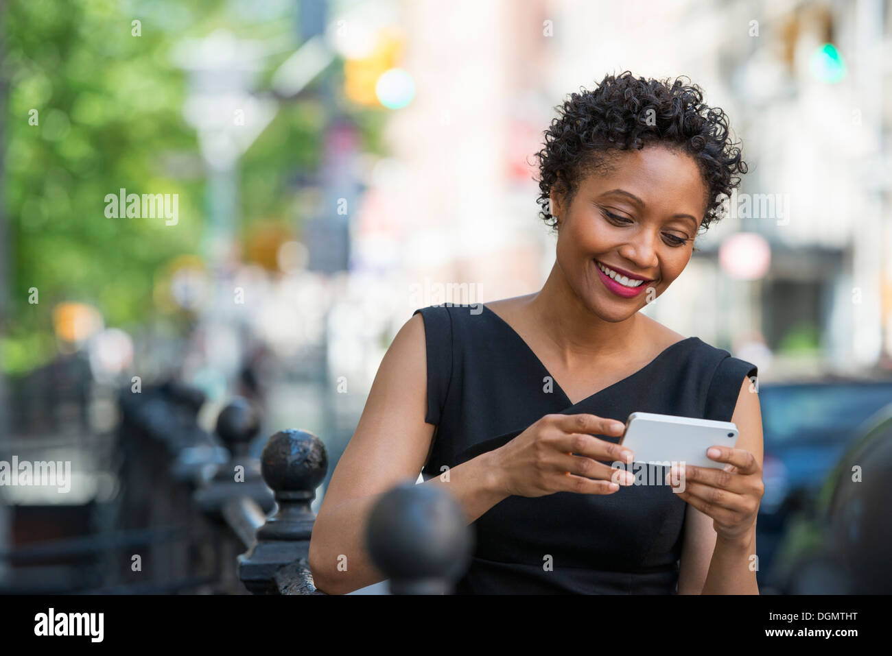 People on the move. A woman in a black dress on a city street, checking her phone. Stock Photo