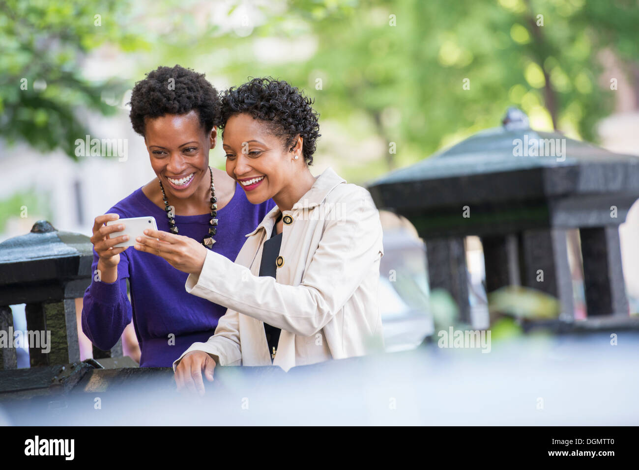 City life. Two women sitting on a park bench, looking at a smart phone. Stock Photo