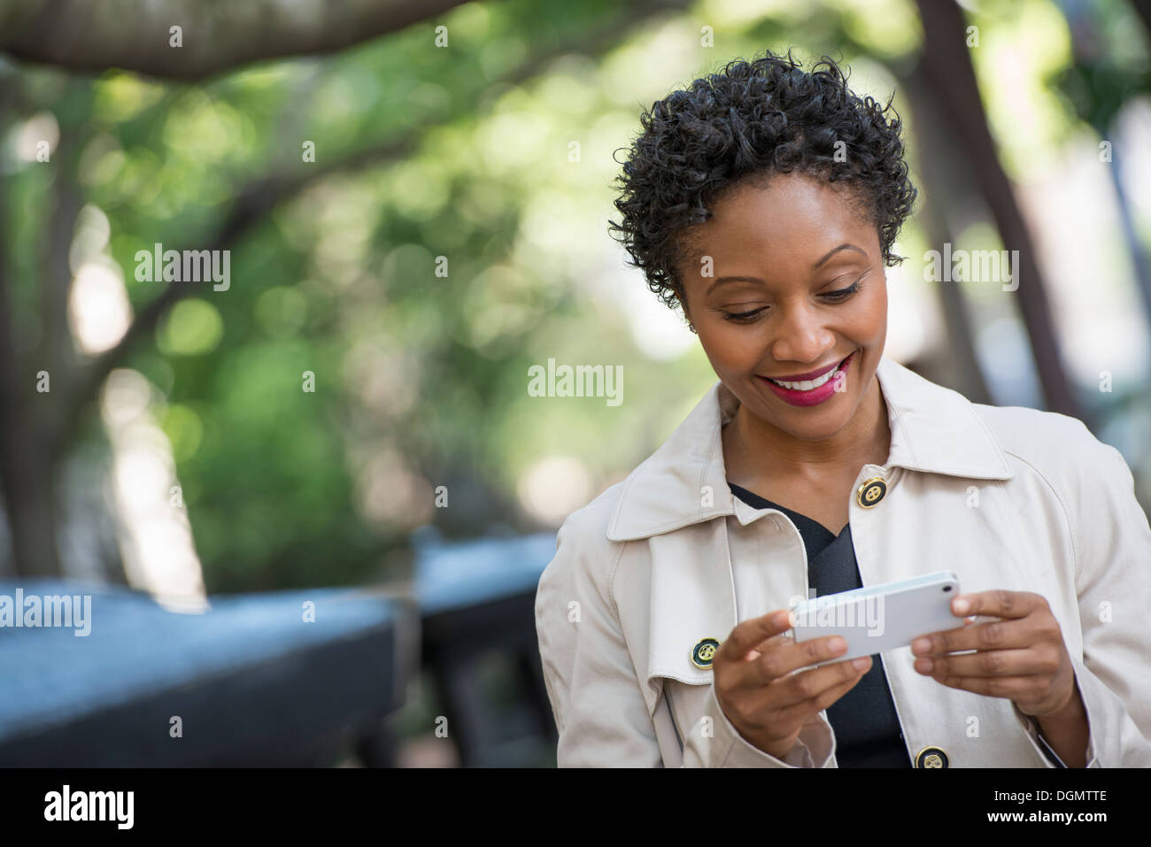 City. A woman outdoors in the park, checking her smart phone. Stock Photo