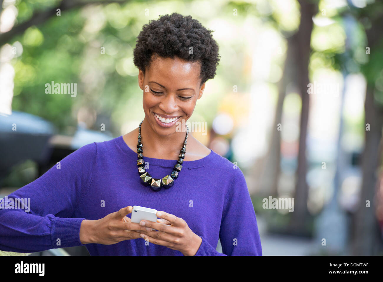 City. A woman in a purple dress checking her smart phone. Stock Photo