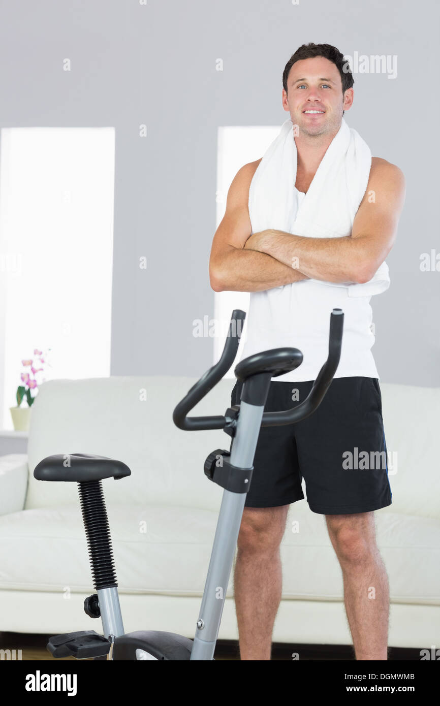 Smiling sporty man standing next to exercise bike cross armed Stock Photo