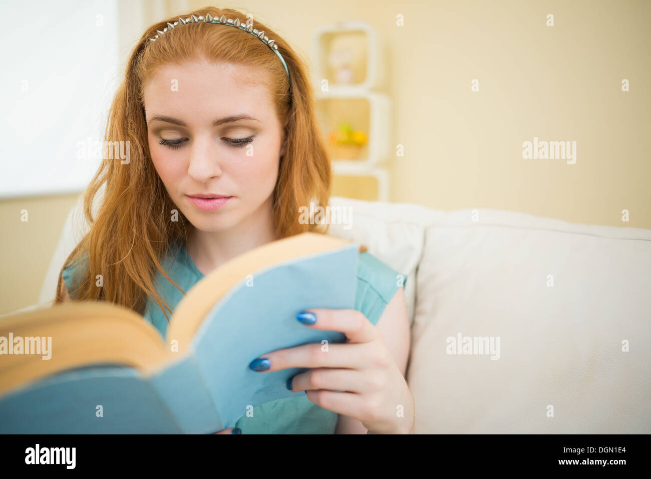 Engrossed redhead reading a book on the couch Stock Photo