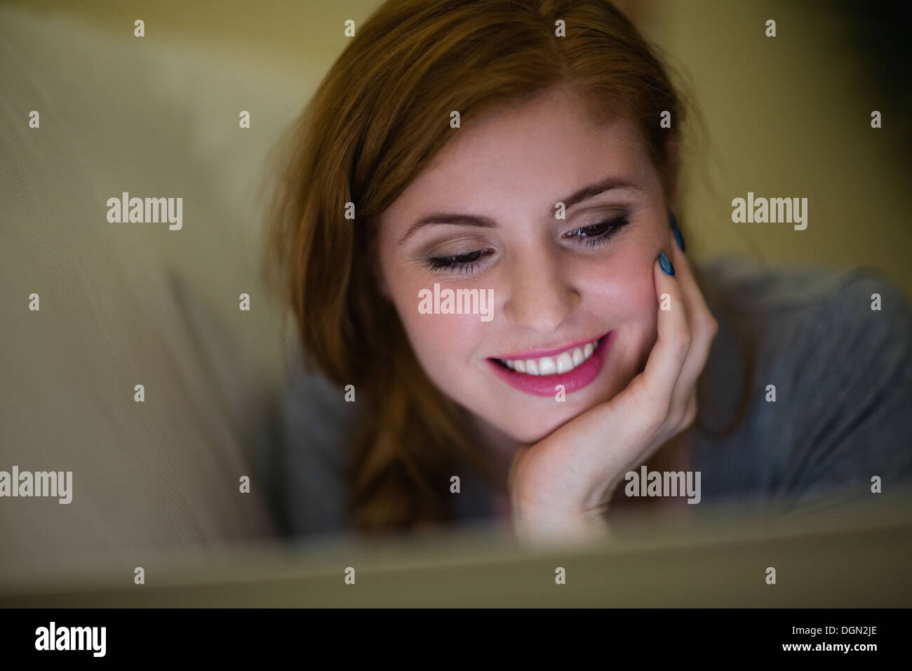 Smiling redhead lying on the couch looking at laptop Stock Photo - Alamy