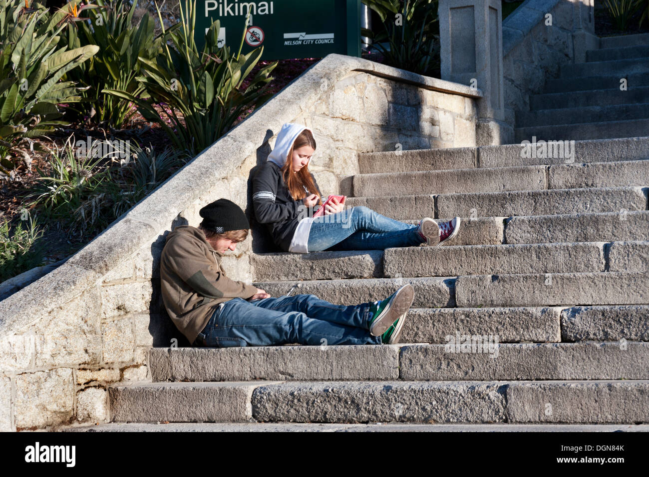 Young people with electronic gadgets relaxing on the steps to the Christ Church Cathedral, City of Nelson, New Zealand Stock Photo