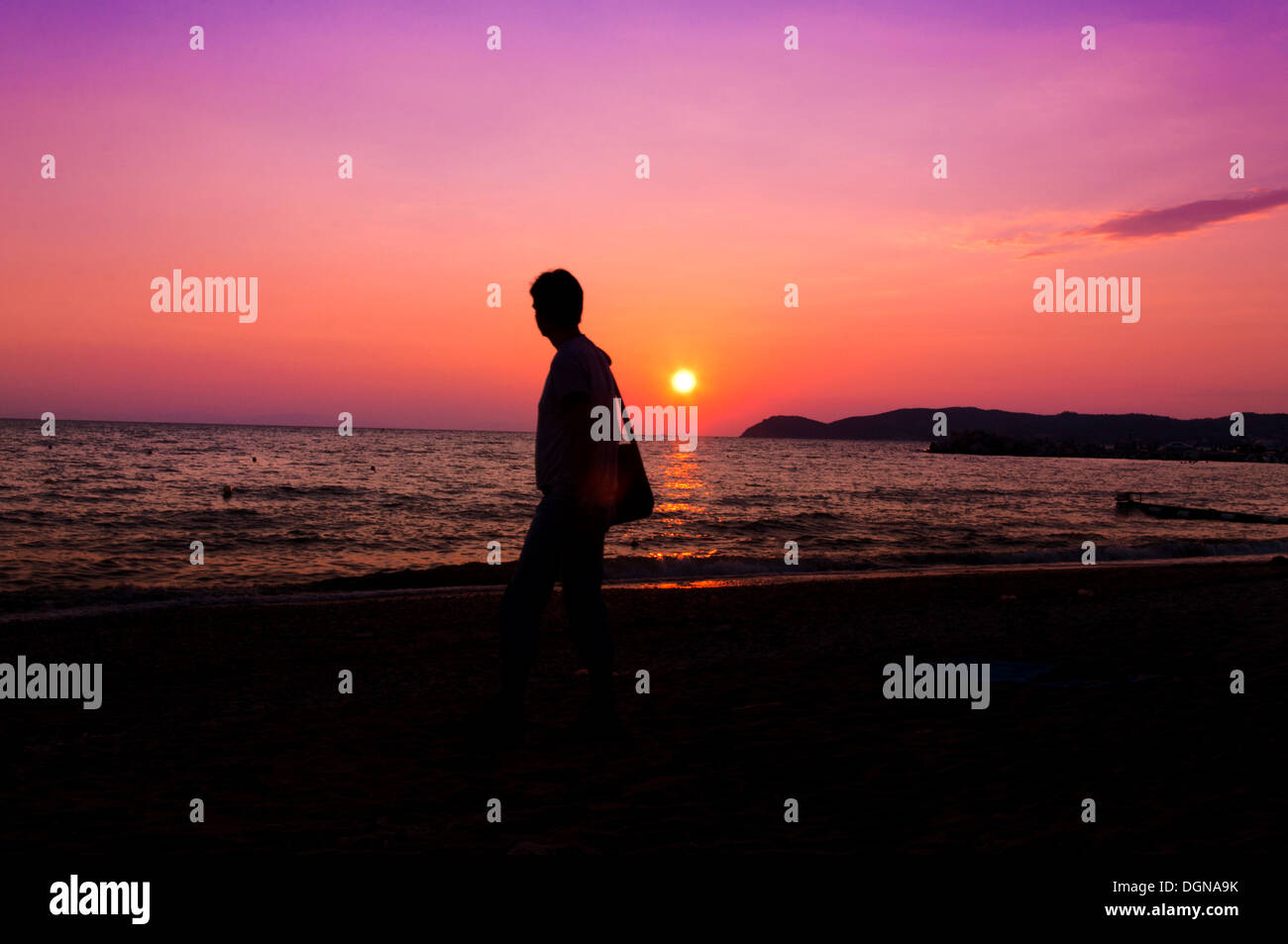 Man walking on the beach with sunset in background Stock Photo - Alamy