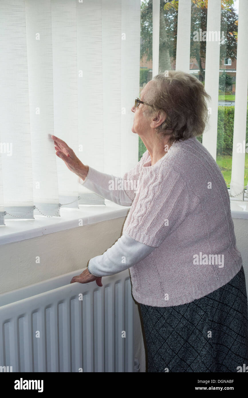 Ninety year old woman with hand on radiator looking out of window. UK. Coronavirus, self isolation, social distancing, quarantine... concept Stock Photo