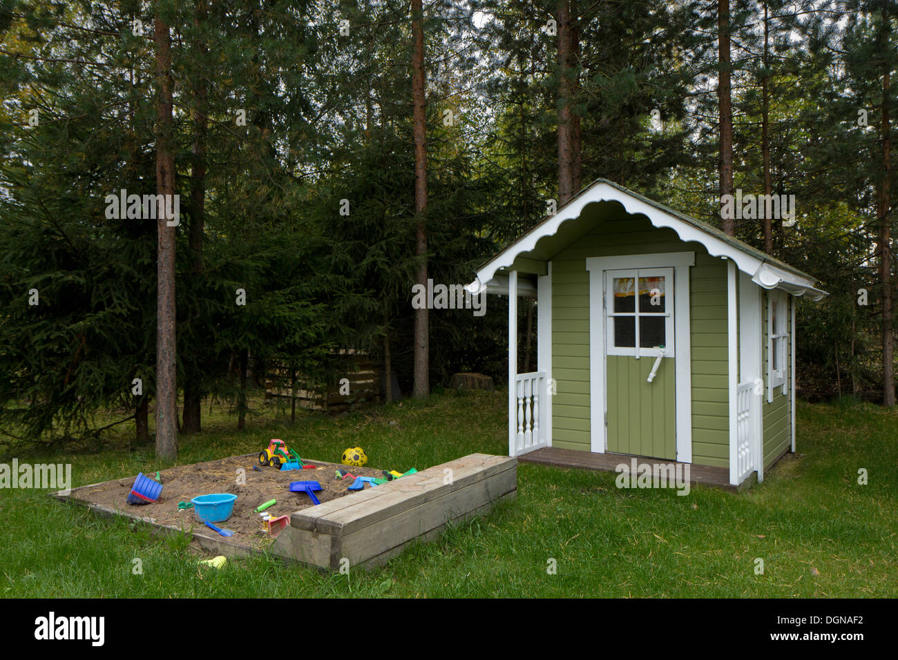 Sandpit and playhouse at desolated backyard in daylight, trees behind them Stock Photo