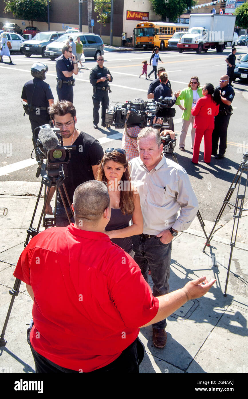Broadcast journalist interviews Hispanic labor demonstration participant on Los Angeles street has her video cameraman records. Stock Photo