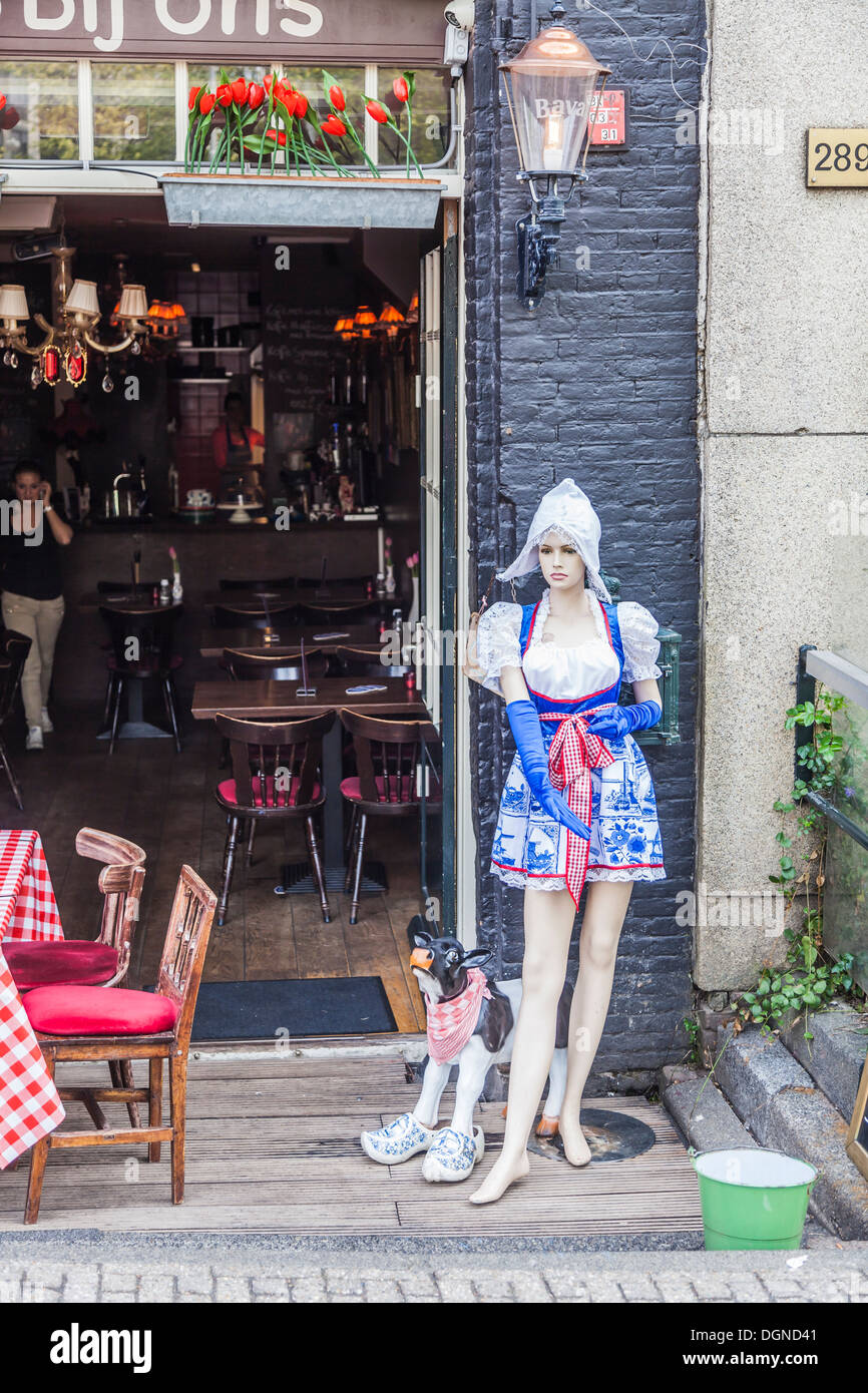 Mannequin wearing traditional Dutch national costume outside a restaurant in Amsterdam, Holland, with a model cow in clogs Stock Photo