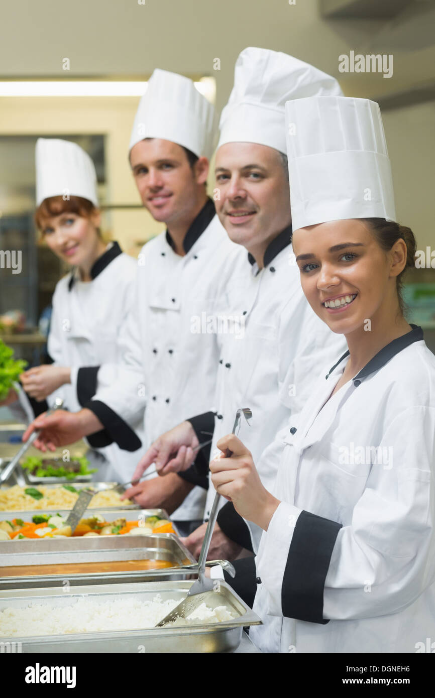 Four chefs working at serving trays smiling at camera Stock Photo