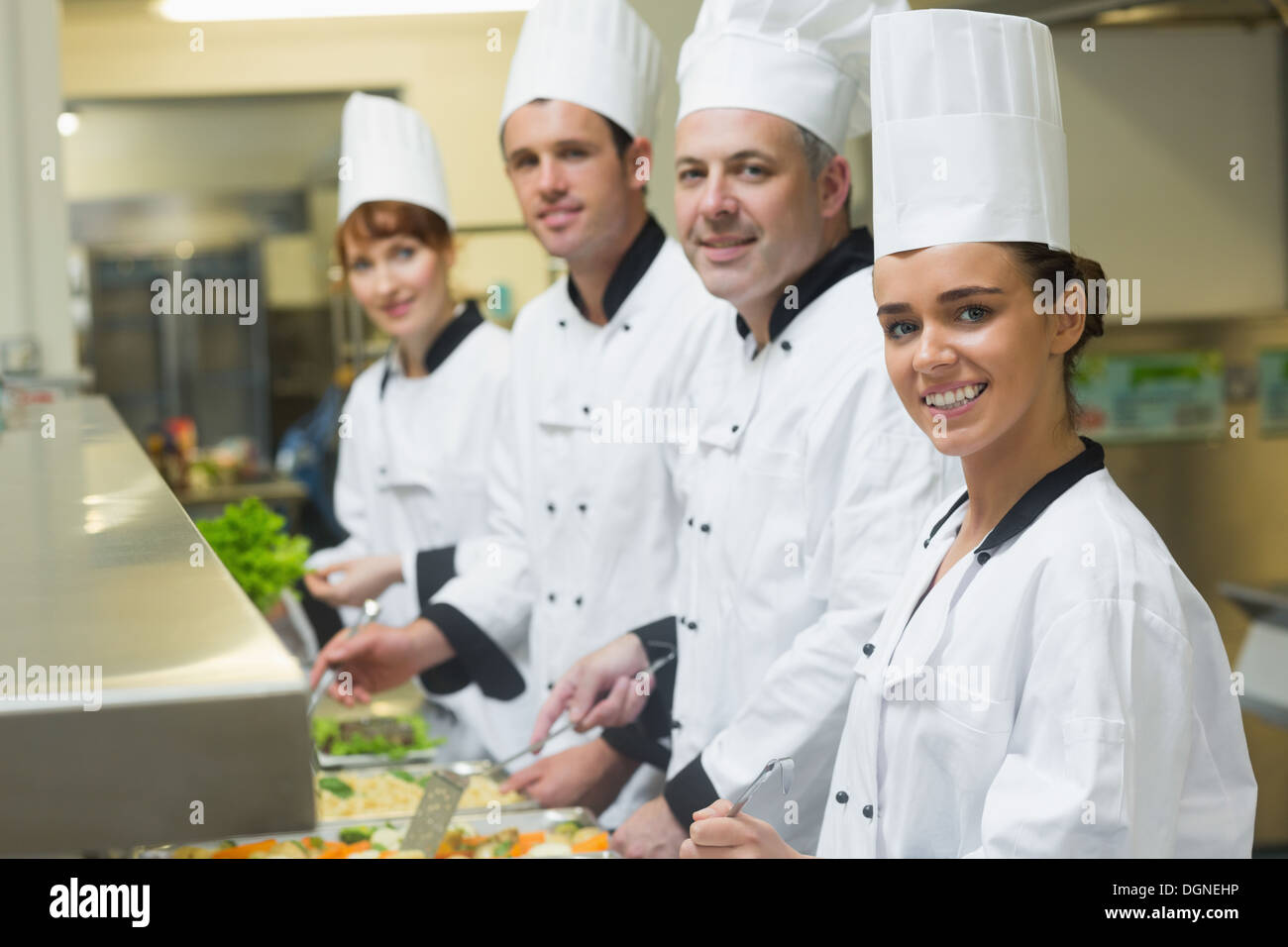 Four chefs smiling at camera while working at serving trays Stock Photo