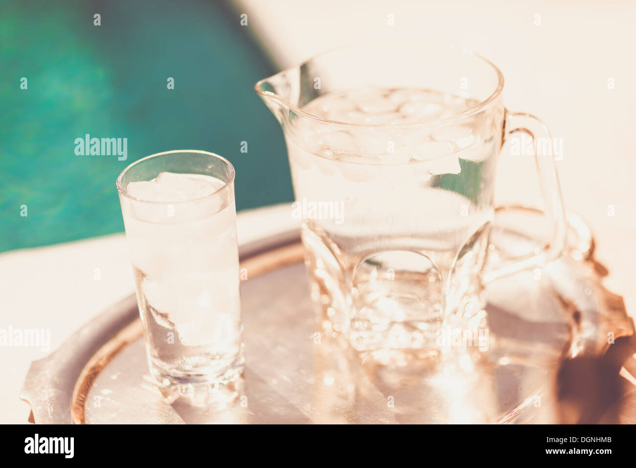 Glass cup and jug of cold water on a silver tray next to pool Stock Photo