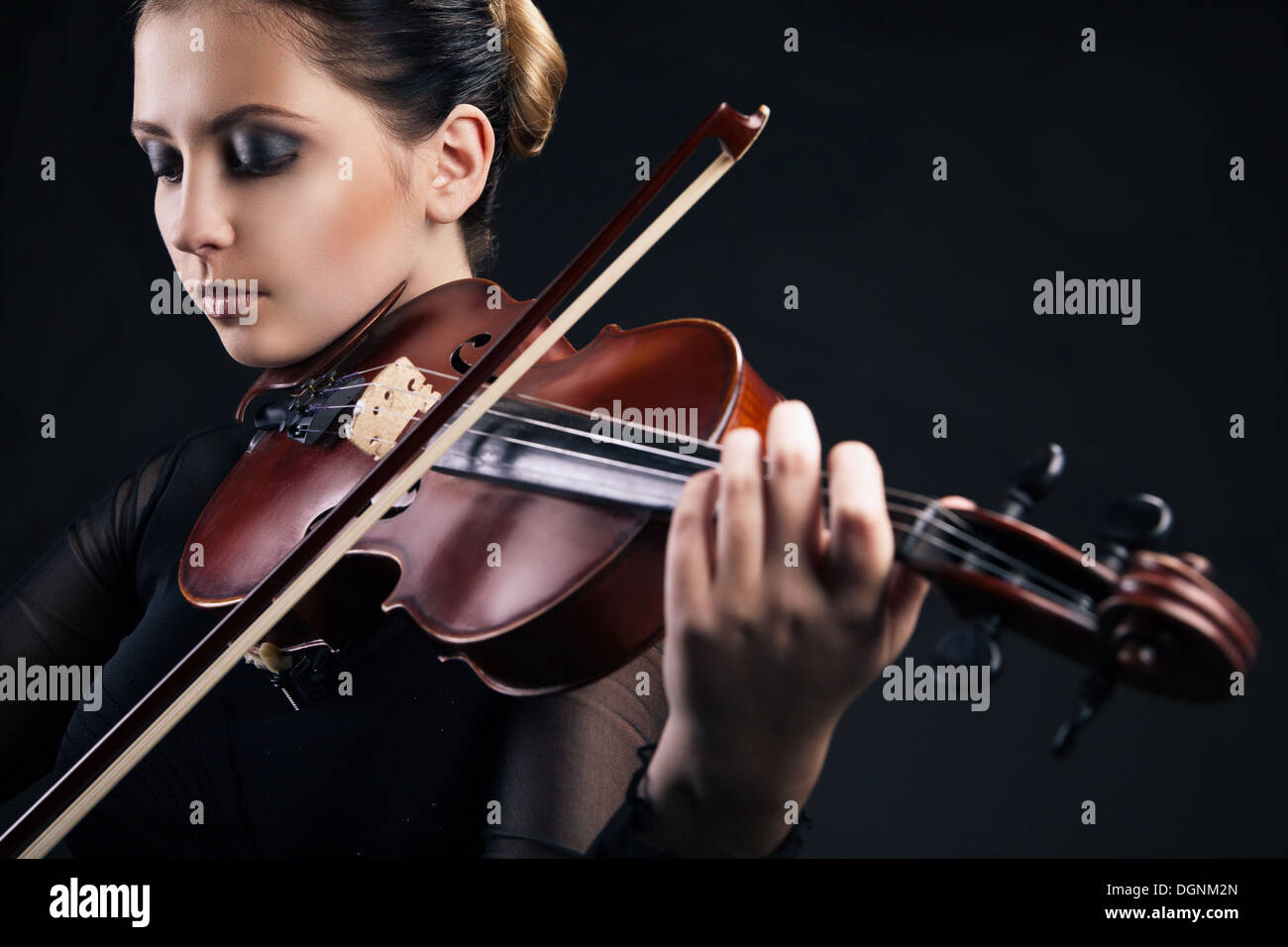 Beautiful young woman playing violin over black Stock Photo - Alamy