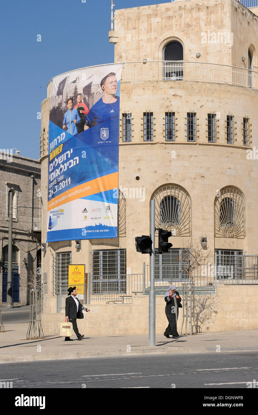 Contrast of modern advertising posters and Orthodox Jews at the corner of Ha Tsanhanim and Shivtei Israel, Jerusalem, Israel Stock Photo