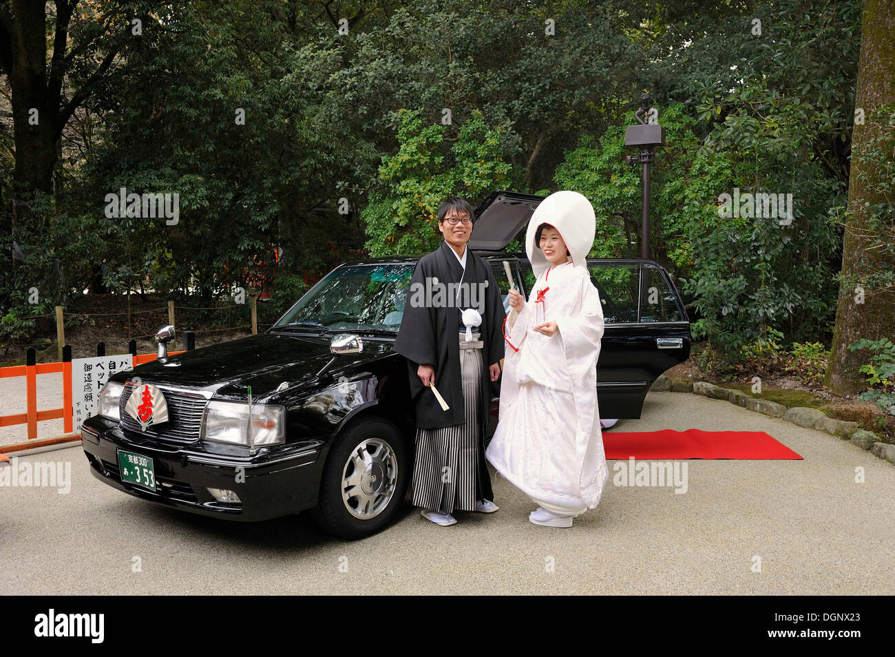 Japanese couple in kimonos, with bridal hood and kimono with brocade, standing in front of the wedding car with a red carpet Stock Photo