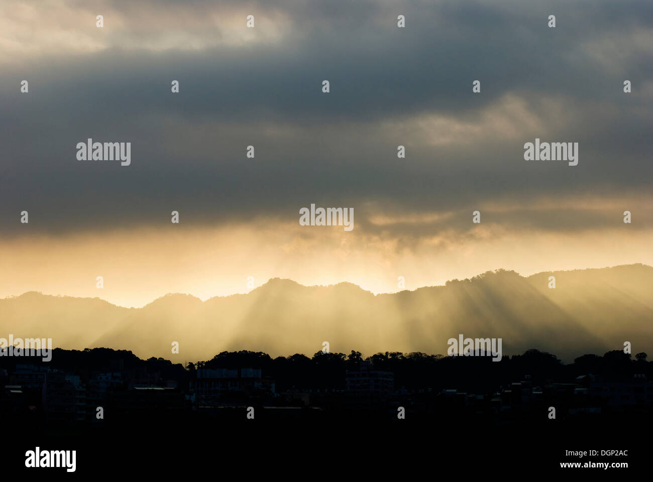 Sunshine coming through gray clouds above mountains Stock Photo