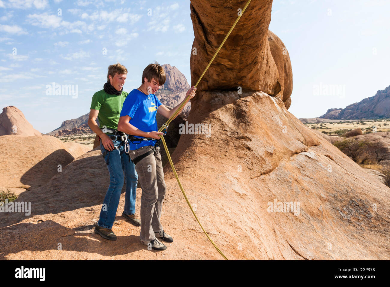 Young men hanging in a climbing rope, Bogenfels, Spitzkoppe, Namibia, Africa Stock Photo