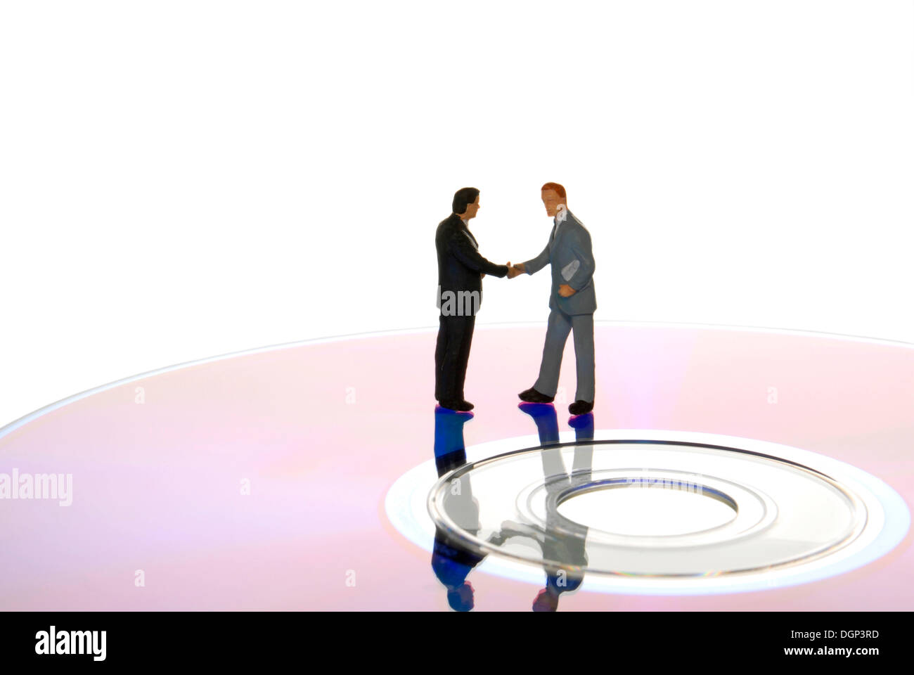 Miniature businessmen figures shaking hands while standing on a data CD Stock Photo