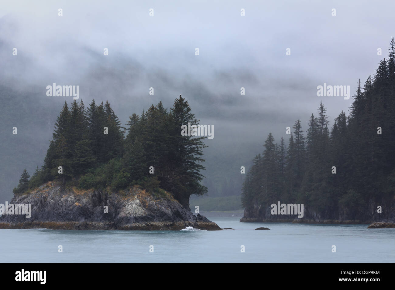 Fog clears around island of pine trees in Alaska Stock Photo