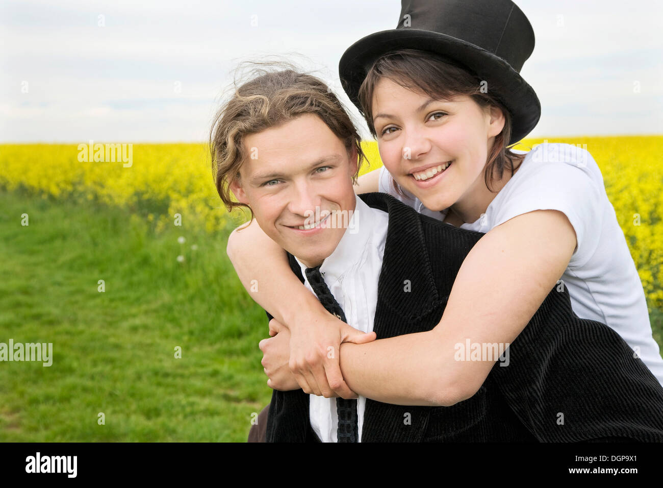 Young woman with top hat embracing her boyfriend who carries her on his