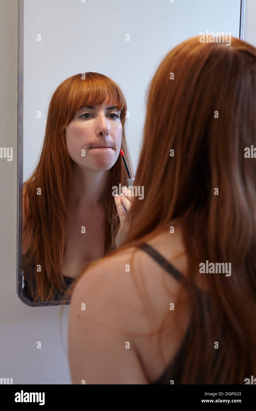 Mid adult woman applying lip gloss in mirror Stock Photo