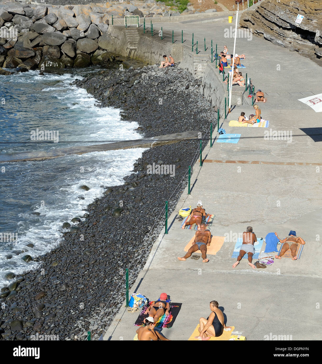 Funchal Madeira. Tourists and locals sunbathing on the concrete path an alternative to the pebble beach. Stock Photo