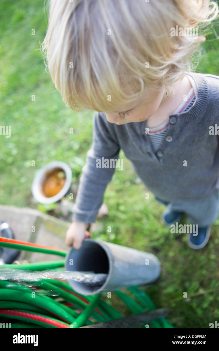 A little boy standing at a garden hose making water pass through a tube