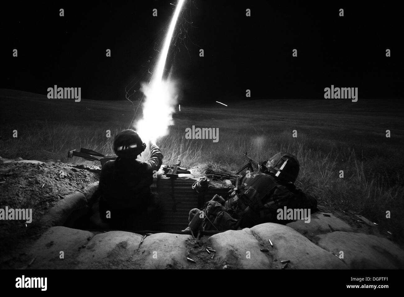 2 British soldiers in a trench at night firing automatic rifles and a flare across open grass land with some tracer fire in shot Stock Photo