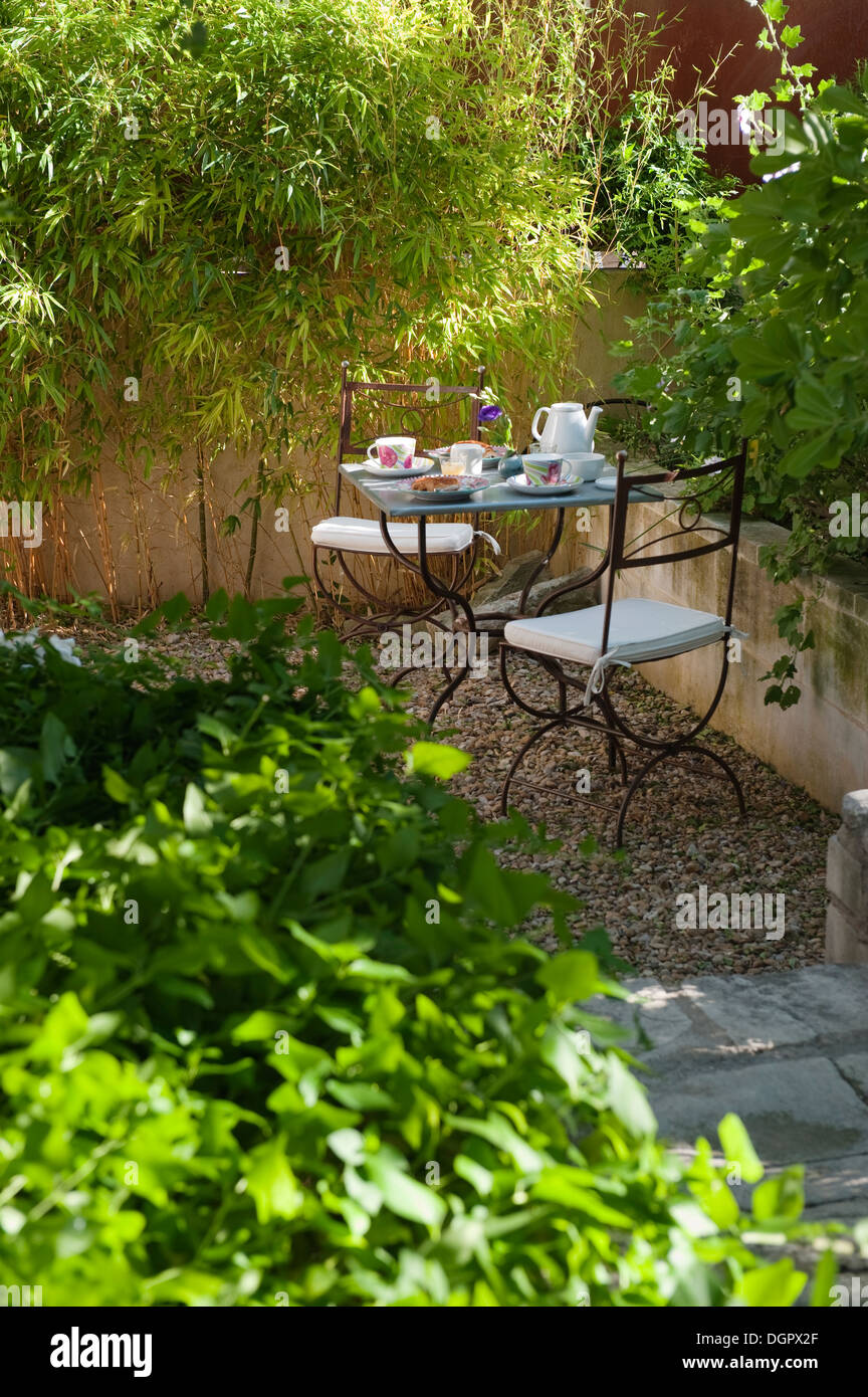 Wrought iron cafe table and chairs laid for tea in garden courtyard. Stock Photo