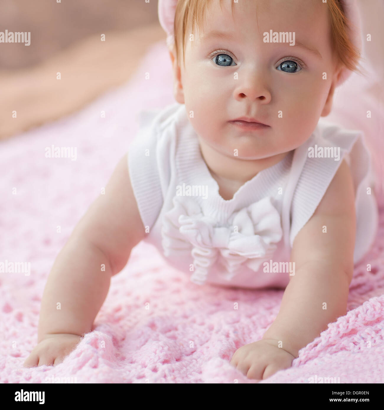 Sweet little baby girl lying on her tummy wearing a white jacket and