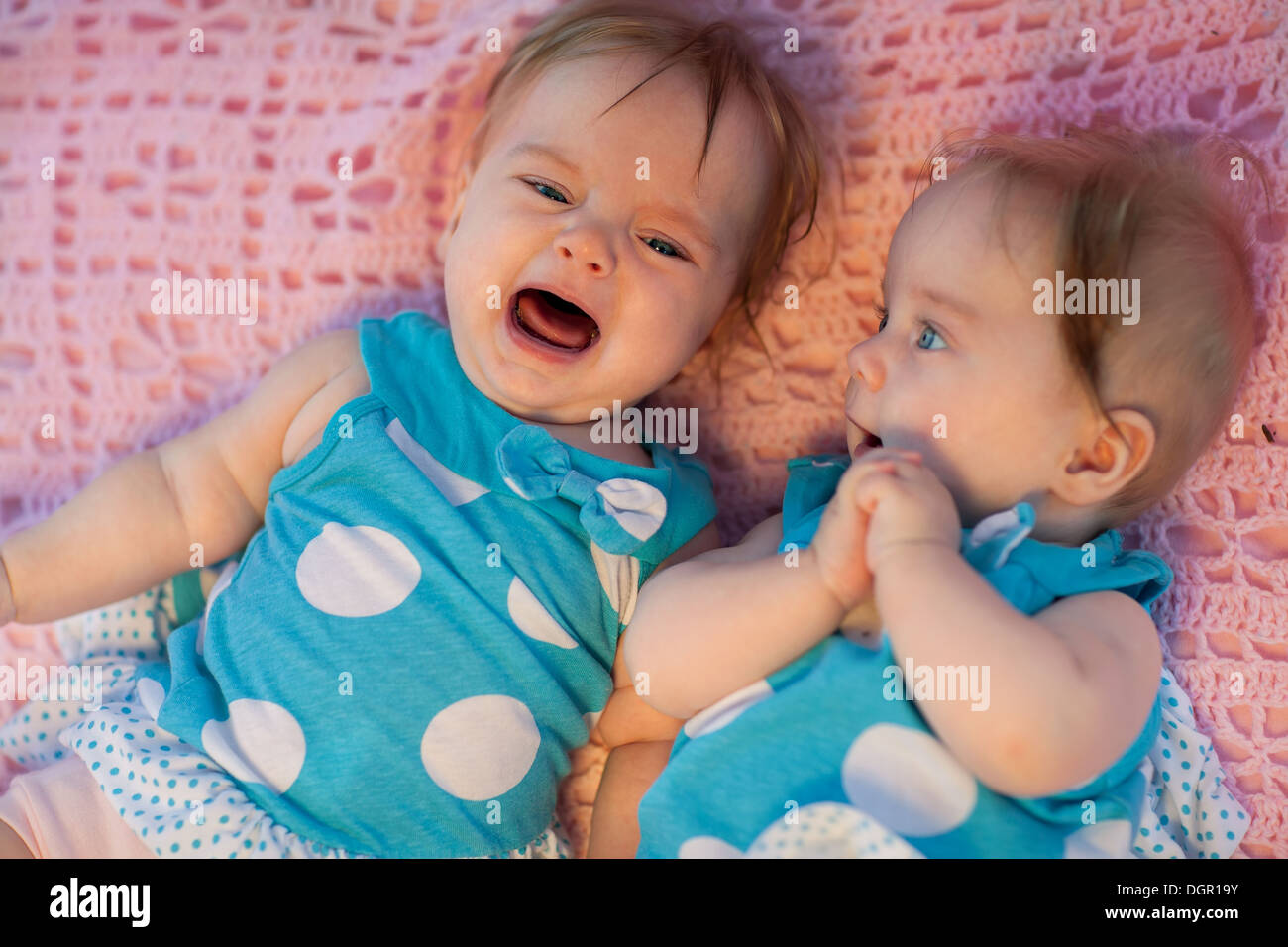Sweet little twins lying on a pink blanket. They in blue dress with white polka dots. Stock Photo