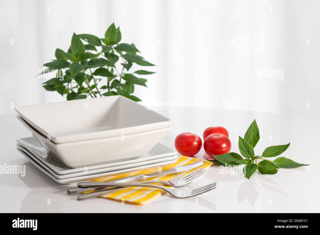 Plates, kitchen utensils, herbs and tomatoes on a white table Stock