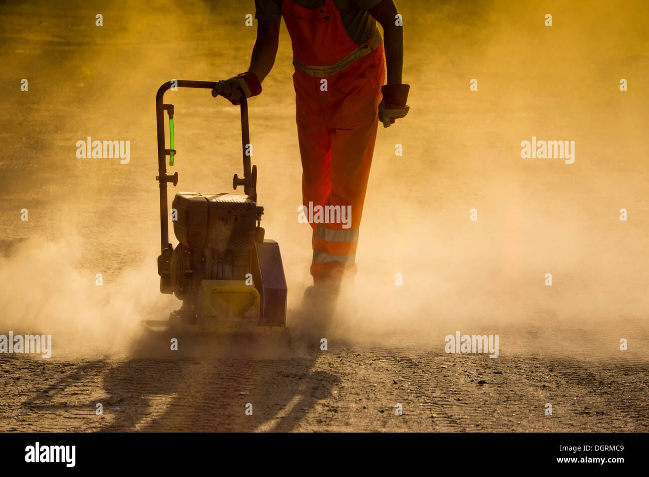 Road worker operating a plate vibrator to compress a dusty road, Hesse, PublicGround Stock Photo