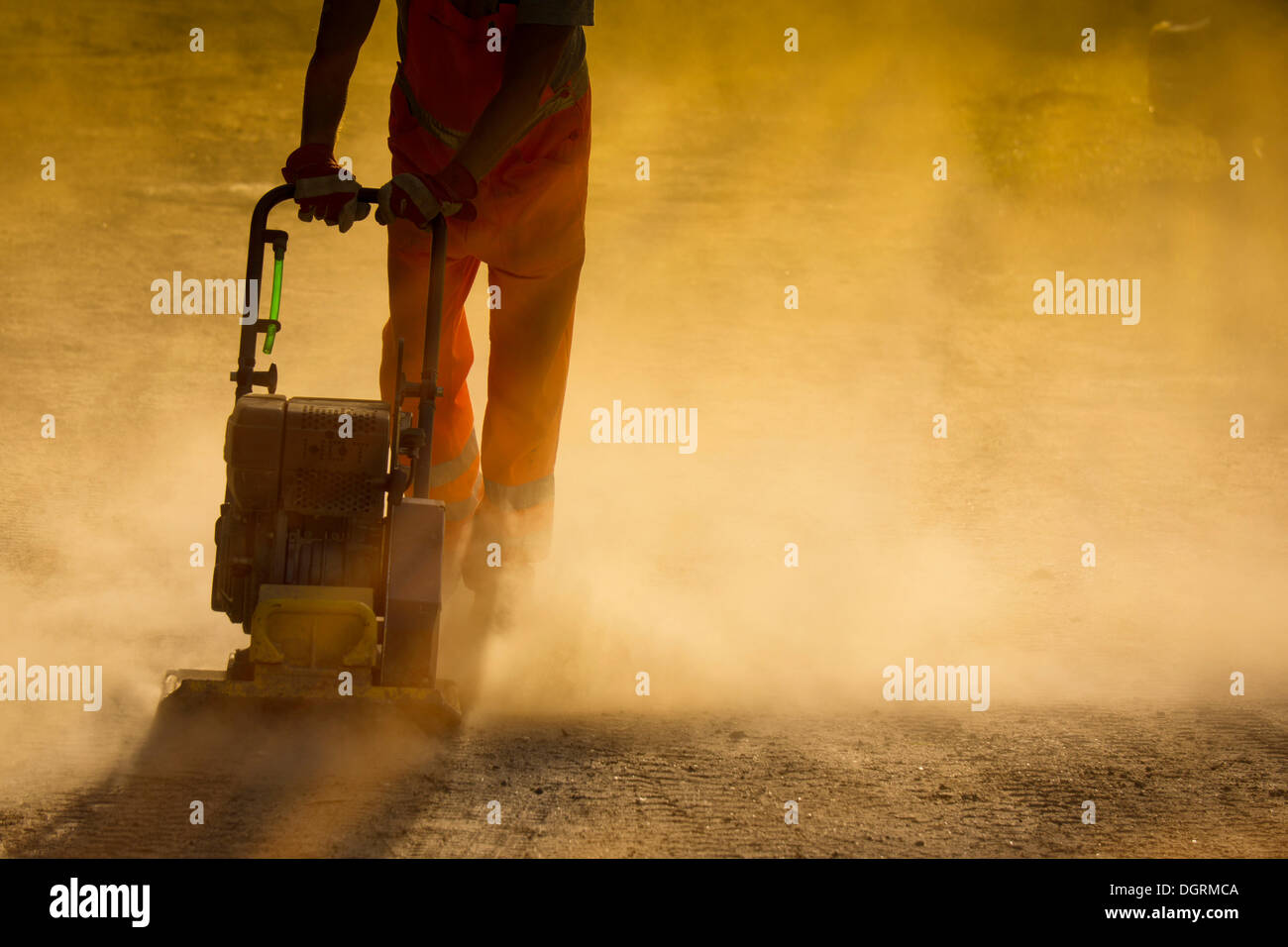 Road worker operating a plate vibrator to compress a dusty road, Hesse, PublicGround Stock Photo