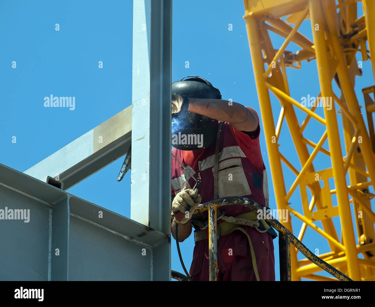 welder with protective mask welding metal construction, yellow crane on his back Stock Photo