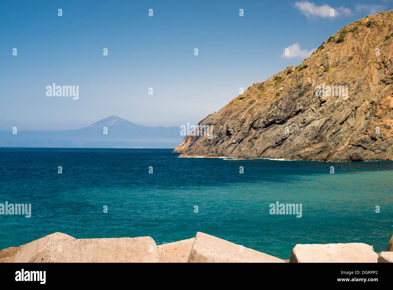 Coastal defence and rocky cliffs at Playa de Vallehermoso, La Gomera, with Teide Volcano on Tenerife visible in the background Stock Photo