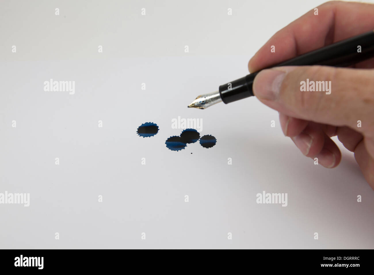 Hand holding a fountain pen, blue ink drops on paper Stock Photo