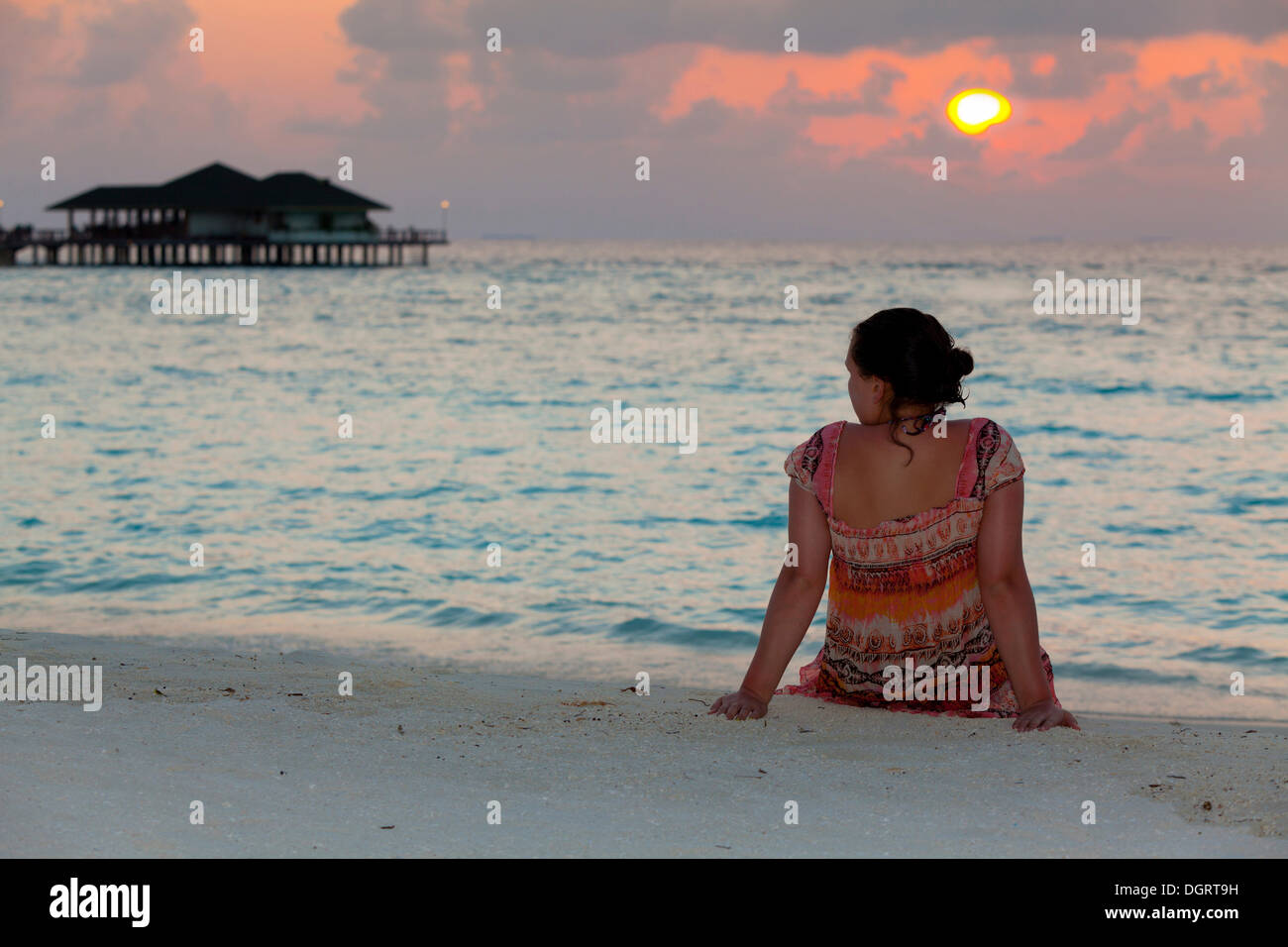 A girl, about 15 years old, sitting on the beach watching the sunset, North Male Atoll, Republic of Maldives, Indian Ocean, Asia Stock Photo