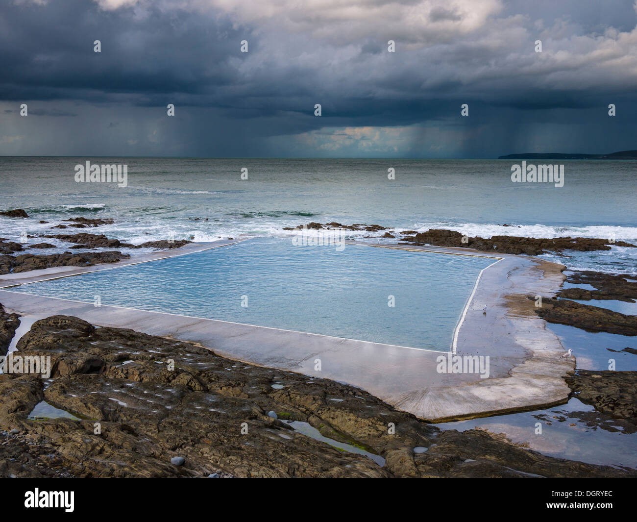 The Rock Pool swimming pool at Westward Ho! and a summer rainstorm over the Atlantic in the distance on the North Devon Coastline, England. Stock Photo