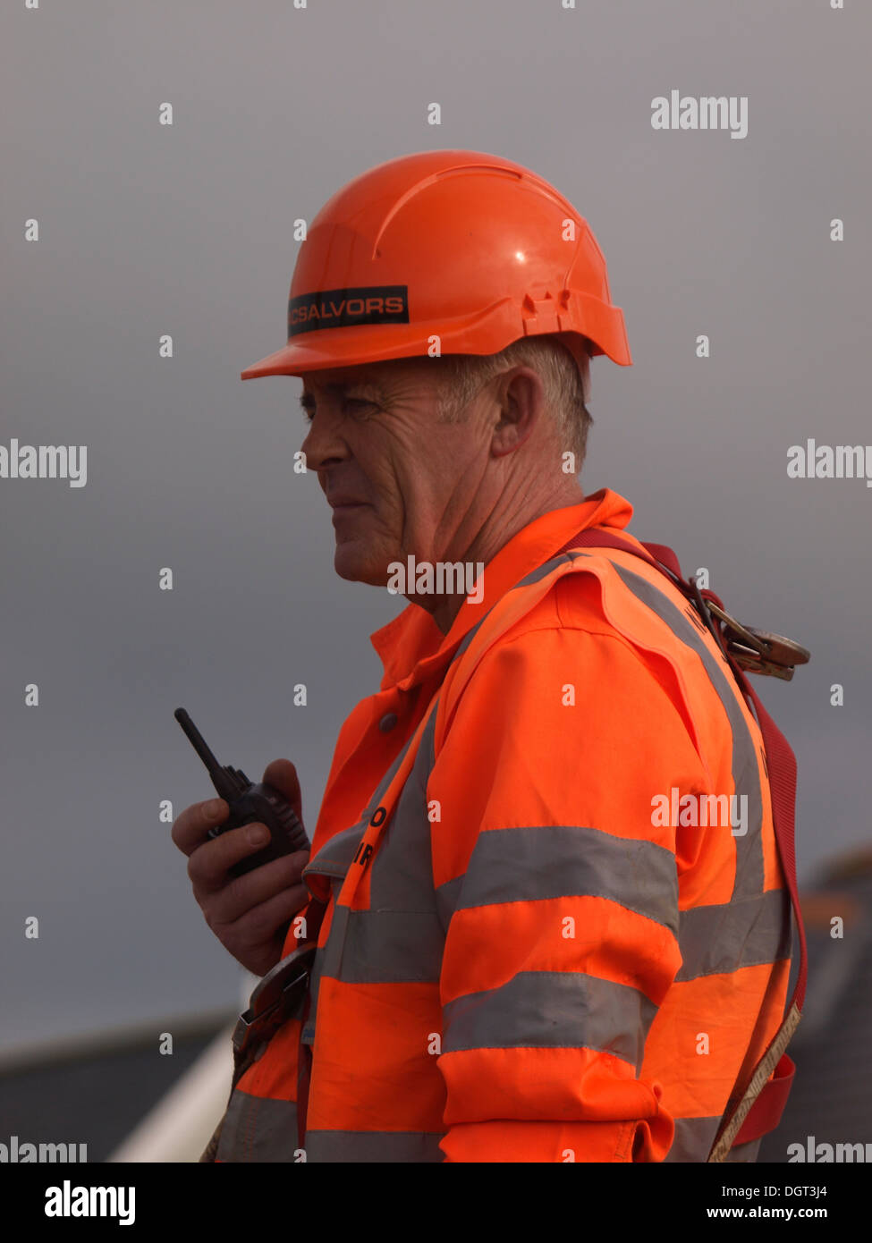 mature construction worker with walkie talkie directing crane operator, UK Stock Photo