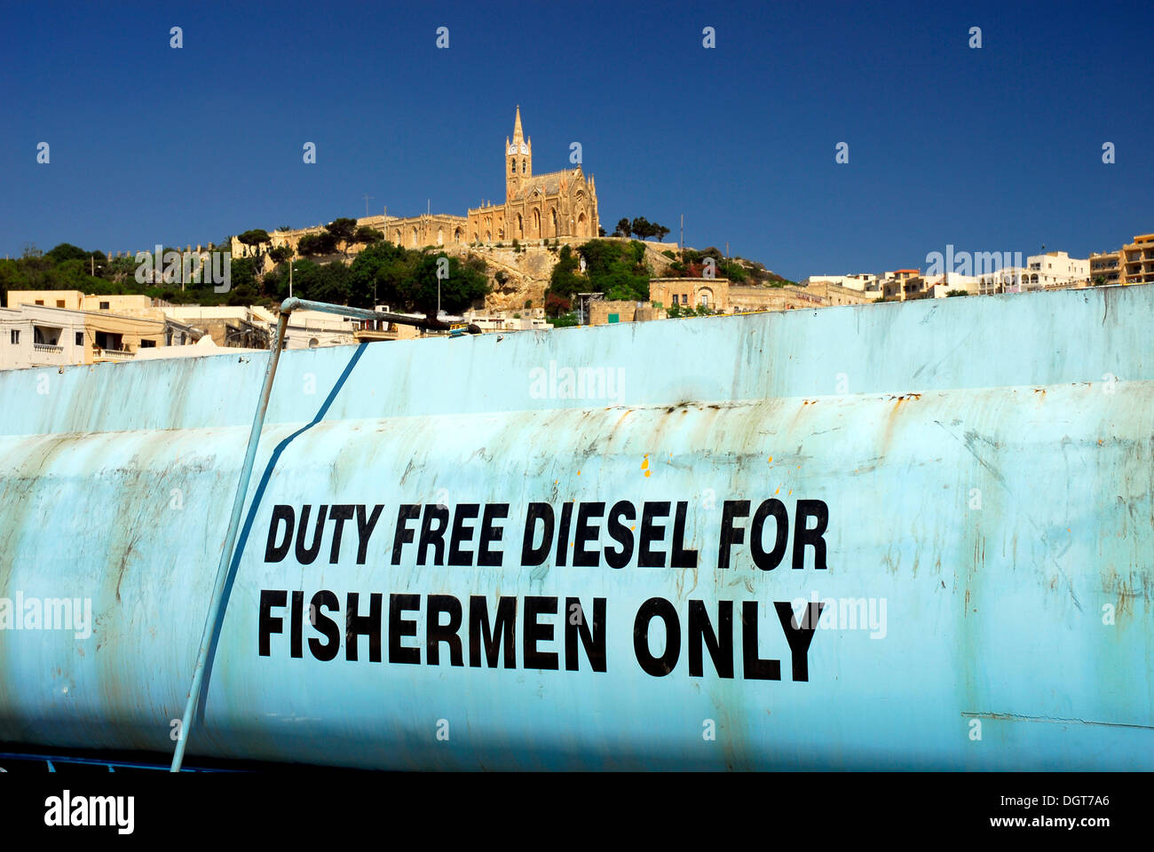 Blue tank containing diesel fuel, duty free diesel for fishermen only, Mgarr Harbour, church at back, Mgarr, Island of Gozo Stock Photo