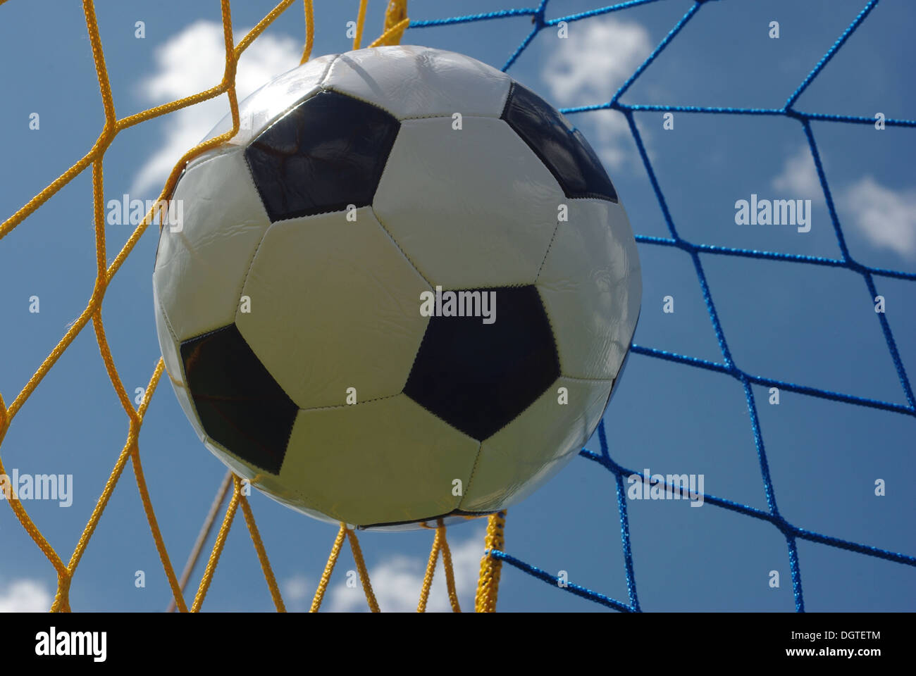 the foot ball in mesh of goal on background of clouds Stock Photo
