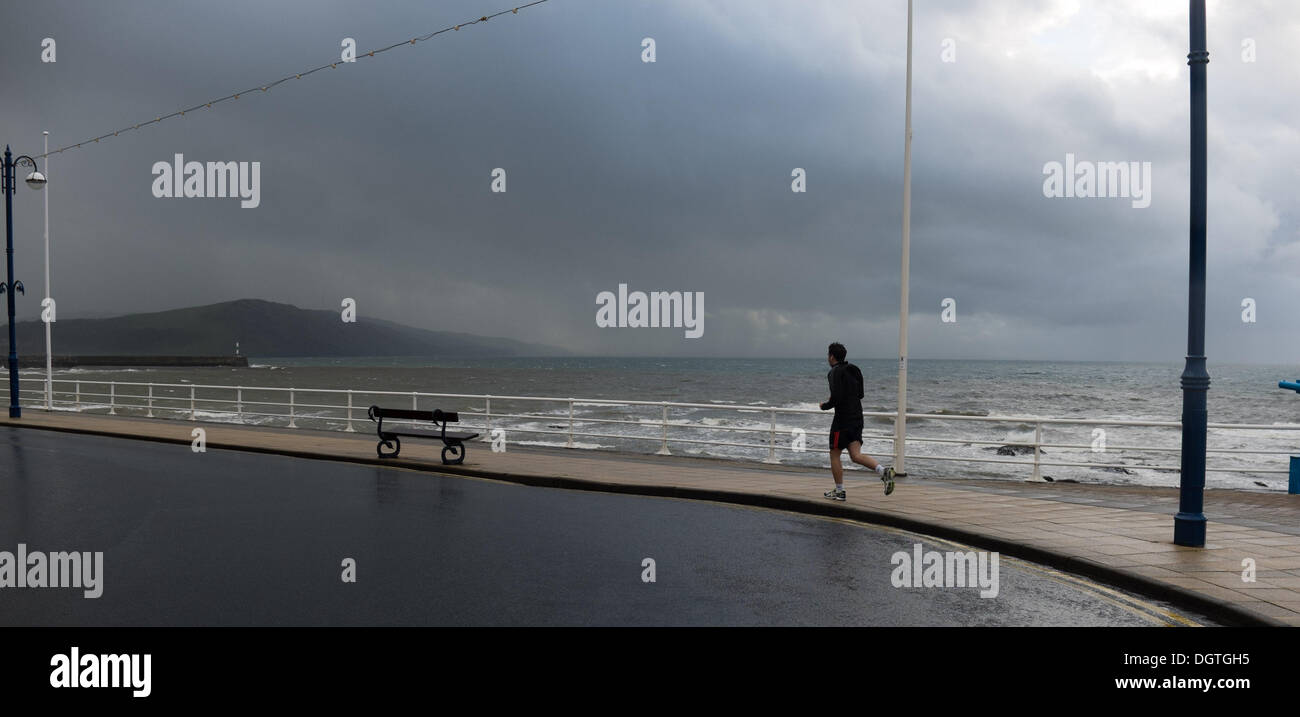 Aberystwyth Wales UK, October 25 2013 A man jogging along the seafront as heavy thundery rain sweeps in off the sea at Aberystwyth in the west wales coast. The weather in the west and south of the UK is expected to turn dramatically stormier over the next 48 hours, with winds of up to 90mph forecast for many southern counties photo Credit:  keith morris/Alamy Live News Stock Photo