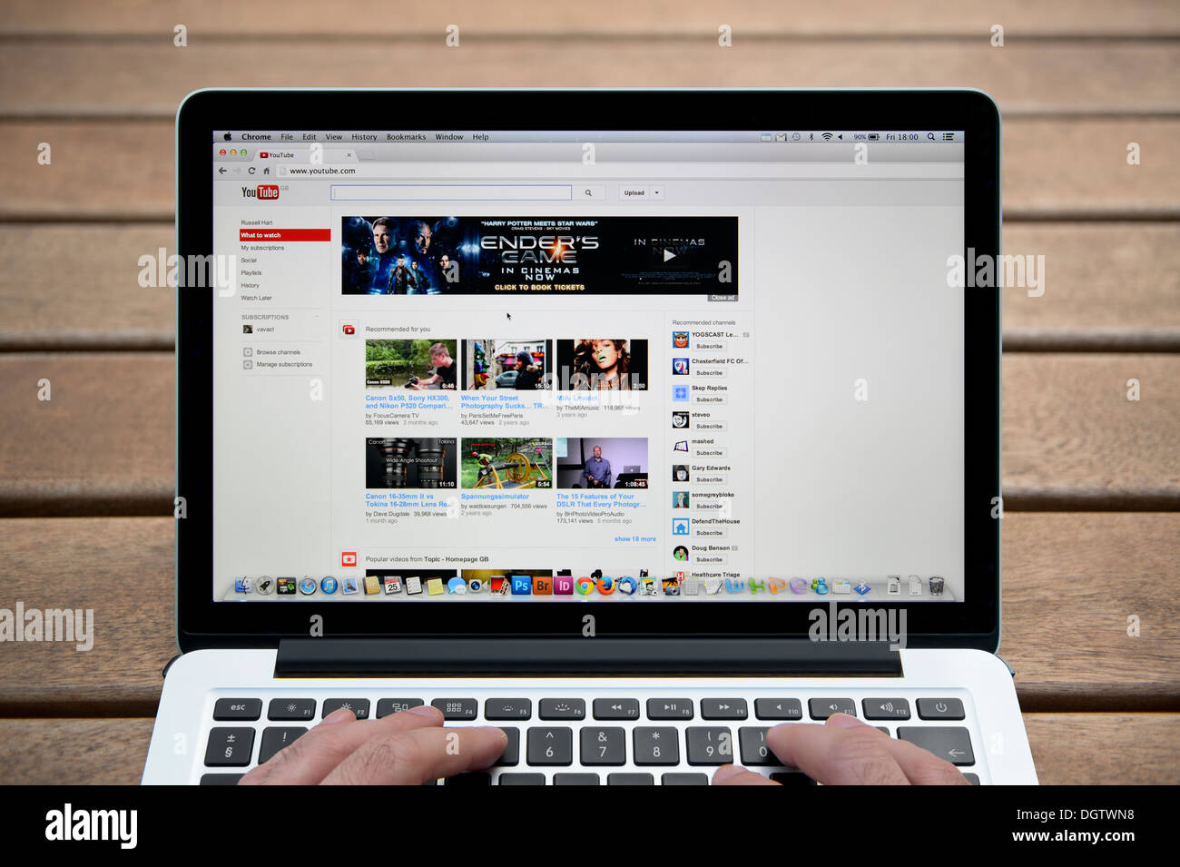 The YouTube website on a MacBook against a wooden bench outdoor background including a man's fingers (Editorial use only). Stock Photo