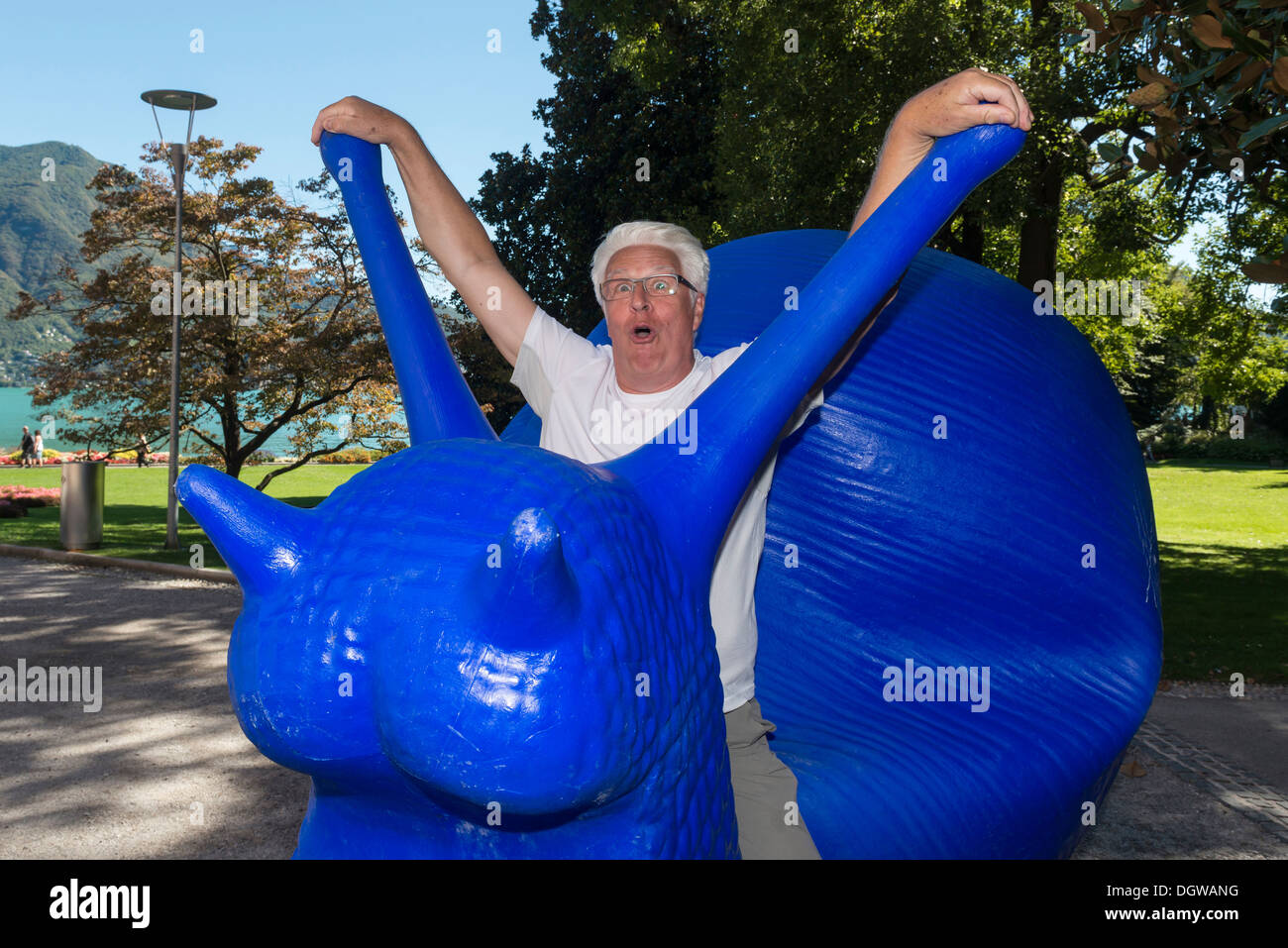 A man pretending to ride a giant blue snail sculpture. Lugano. Switzerland Stock Photo
