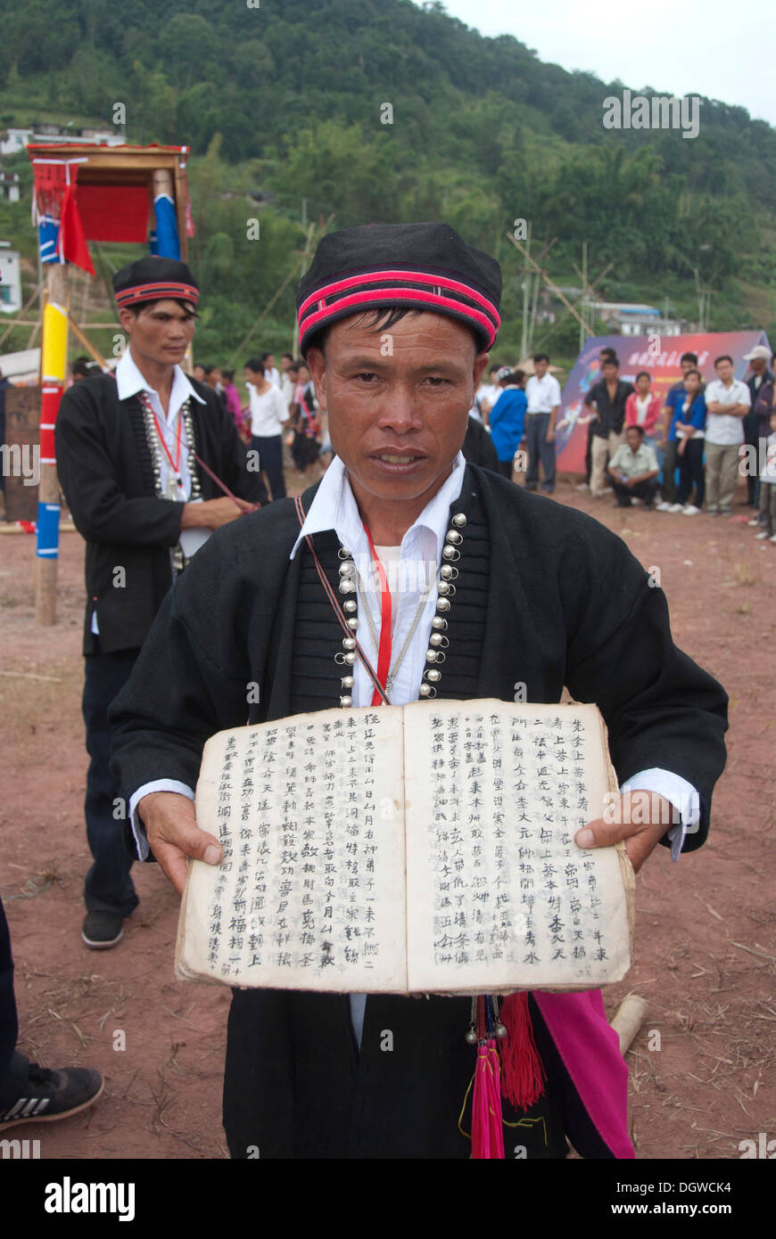 Ethnic festival, man of the Yao minority in traditional costume presenting book and writing, Jiangcheng, Pu'er City Stock Photo