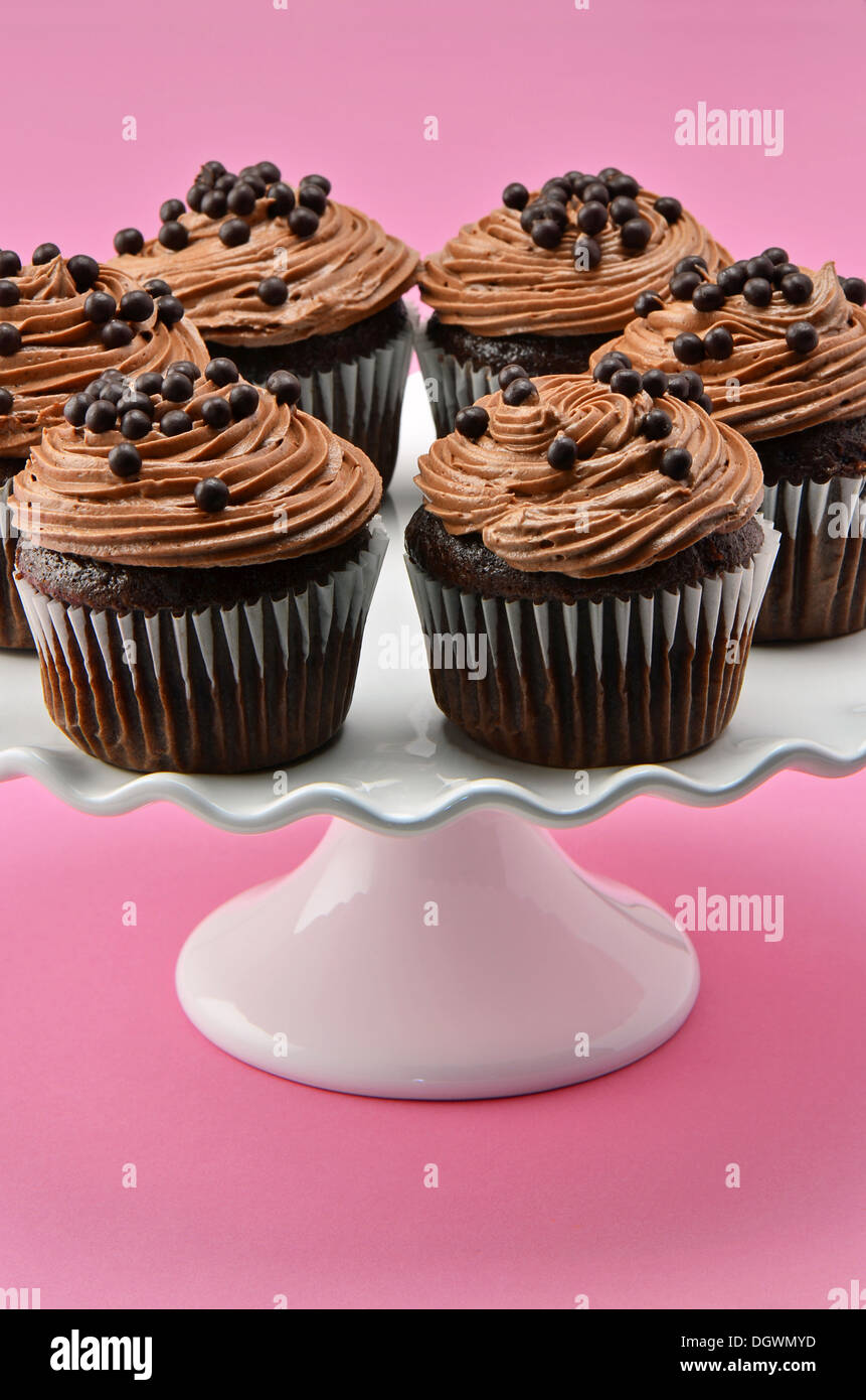 Gourmet chocolate cupcakes with chocolate chiffon icing and chocolate balls on white cake stand with a deep pink background Stock Photo